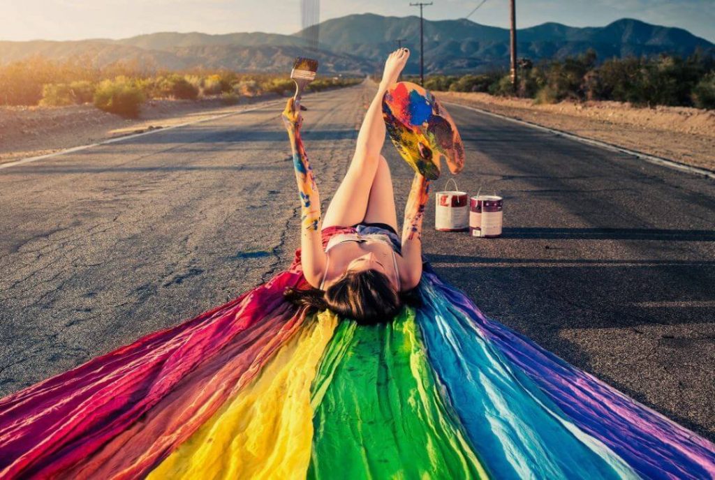 woman laying freely on road with palette of rainbow colors, symbolizing she's pursuing what she's passionate about: painting