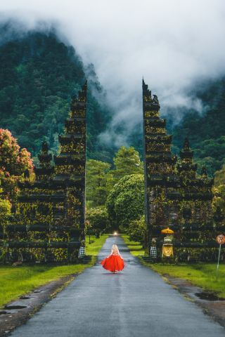 Woman in a red dress about to walk through a giant gate, symbolizing you can start your journey to learn how to stop doubting yourself.